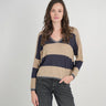a woman wearing a beige and navy stripe sweater and black jeans on a neutral background