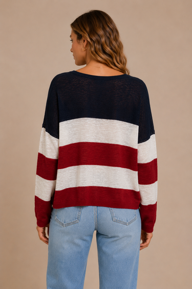 Person wearing a black, red, and white striped sweater with blue jeans on a beige background