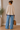 a woman wearing a beige sweater with a white stripe on the collar and a blue stripe at the bottom hem with a slip at hips and blue jeans on a neutral background