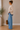 A woman wearing a beige sweater with a blue stripe with a side split at the hem at the bottom and jeans