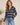 A woman wearing a navy blue and beige striped long-sleeve henley sweater with light blue jeans, standing in a softly lit indoor setting.