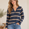 A woman wearing a navy and beige striped long-sleeve henley sweater with blue jeans, standing in a brightly lit indoor setting.