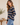A woman wearing a navy blue and beige striped long-sleeve henley sweater with light blue jeans, standing in a brightly lit indoor setting.