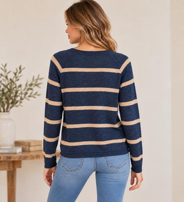 A woman shown from the back wearing a navy blue and beige horizontally striped long-sleeve knit sweater with light blue jeans, standing in an indoor setting.