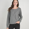 A woman modeling a heather gray long-sleeve henley top with a buttoned neckline, paired with black pants, against a light gray studio background.