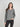 A woman modeling a heather gray long-sleeve henley top with a buttoned neckline, paired with black pants, against a light gray studio background.