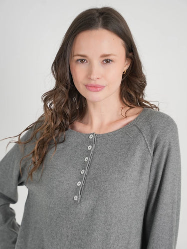 A woman modeling a heather gray long-sleeve henley top with a button placket Against a light grey studio wall