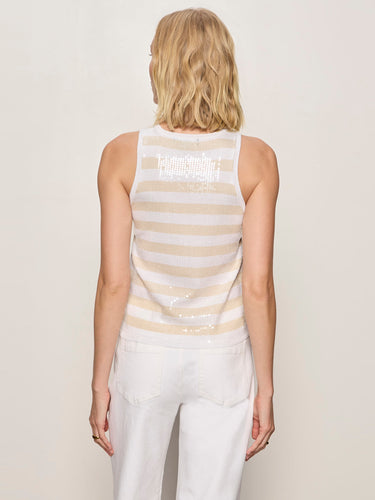 A woman wearing a striped beige and white sequin top with white pants on a neutral background 