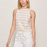 A woman wearing a striped beige and white sequin top with white pants on a neutral background 