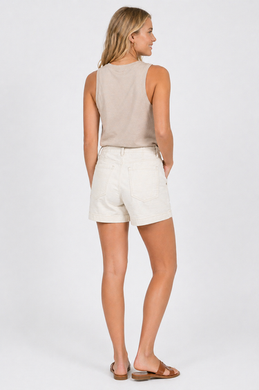 Woman wearing a beige sleeveless top and white shorts on a plain background