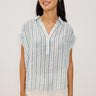 Woman wearing a striped shirt and white pants against a plain background