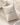 A two-tone silver and gold ceramic bracelet displayed on a cream-colored fabric pillow, set against a textured beige background with dried floral elements.