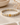 A beaded stretch bracelet with alternating white, beige, and gold ceramic beads, featuring a polished gold rectangular clasp, displayed on a textured beige surface with dried flowers and a ceramic bowl in the background.