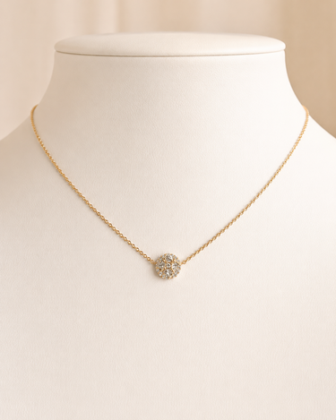 A delicate gold chain necklace with a small round pavé pendant, displayed on a cream-colored jewelry bust.