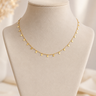 A delicate gold chain necklace with small, evenly spaced flat circular disc charms, displayed on a beige fabric jewelry bust.