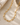 A gold hammered paper clip necklace on a textured surface.