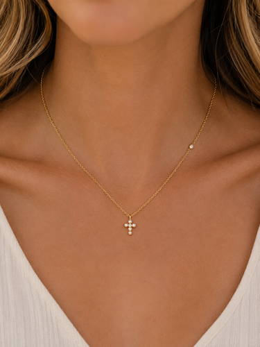 a woman wearing a pearl cross necklace on a gold plated chain