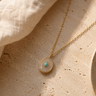 A pearl and opal pendant with a gold chain on a table