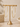A pair of large gold hoop earrings displayed on a matching gold stand, set against a warm beige background with subtle decorative props.