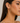 A close-up of a woman wearing large, thin gold hoop earrings, showing the earring on her ear against a soft light gray background.