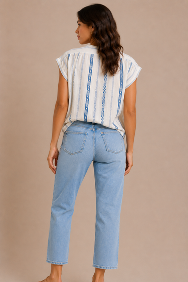 A woman wearing a cotton cream v neck blouse with blue stripes and jeans on a neutral background