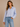 Woman wearing a light blue striped shirt and jeans against a beige background