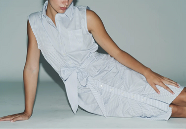 a woman posed on the floor in a blue and white striped shirt dress with a tie waist and ruched front detailing