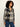 A woman wearing a long-sleeve plaid button-up shirt in black, white, and navy, paired with blue jeans, photographed against a plain off-white studio background.