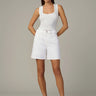Woman wearing a white tank top and shorts on a plain background