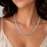 A close-up of a woman wearing a delicate beaded necklace with pale translucent beads and a small cluster of iridescent accent beads at the center, paired with a cream lace-trim camisole.