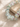 A close-up of a beaded stretch bracelet made of translucent pale blue-green round beads with tiny multicolored spacer beads, resting on a textured beige fabric surface next to a stone.