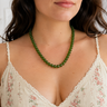 A close-up of a woman wearing a green beaded necklace with matching green hair clips, paired with a cream floral camisole top.