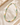 A beaded necklace made of small pastel and green gemstone-like beads with gold-tone clasp, arranged on a soft cream fabric with a stone prop in the corner.