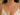 A close-up of a model wearing a delicate gold Y-necklace adorned with small green gemstones, paired with a white floral lace camisole.