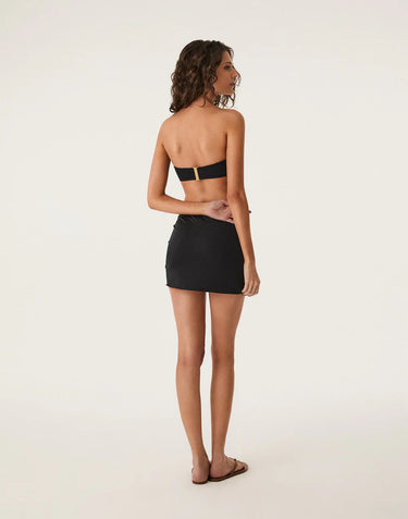 Woman wearing a black strapless bikini top and mesh cover up skirt on a white background