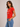 A woman wearing a red baby tee with vacation and meditation written on chest with blue jeans