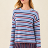 A woman wearing a light blue ribbed knit sweater with horizontal navy and red stripes, paired with a matching striped skirt, against a solid beige background.