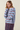 A woman wearing a light blue knit sweater with red and navy horizontal stripes, paired with matching striped trousers, against a plain beige background.