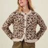 A woman modeling a fuzzy leopard-print cardigan with brown buttons, paired with olive green pants, against a solid light beige background.