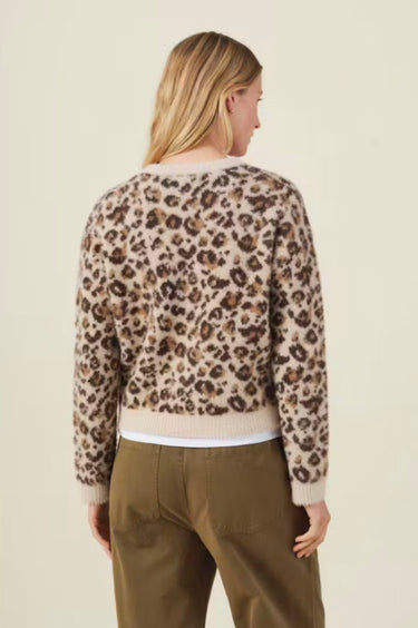 A woman shown from the back wearing a fuzzy knit sweater with a beige, brown, and black leopard print pattern, paired with olive green pants, against a solid light beige background.