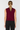 A woman viewed from the back wearing a sleeveless cropped knit top in deep burgundy and black pants, against a plain light gray studio background.