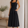 Woman wearing a black dress standing in a minimalistic room with a wooden bench and plant.