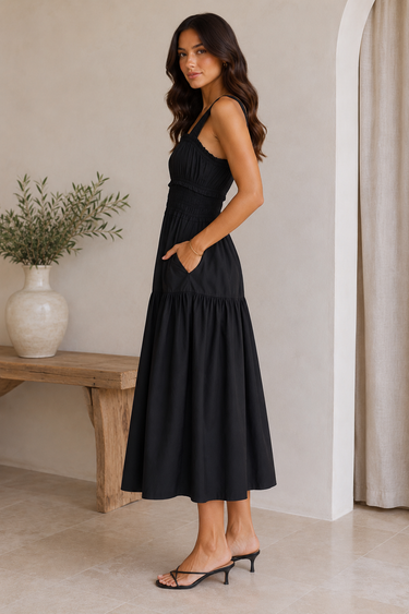 Woman wearing a black dress standing in a room with a wooden bench and plant.