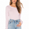 A woman wearing a long sleeve crew neck tee in lavender with blue jeans on a neutral background.