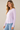 A woman wearing a long sleeve crew neck tee in lavender with blue jeans on a neutral background.