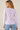 A woman wearing a long sleeve crew neck tee in lavender with blue jeans on a neutral background.