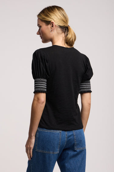 a woman wearing a black blouse with smocked puff sleeves and jeans on a neutral background