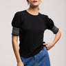 a woman wearing a black blouse with smocked puff sleeves and jeans on a neutral background