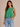A woman wearing a boxy cotton cropped tank in shamrock green and blue jeans on a neutral background