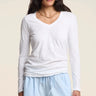 A woman modeling a white long-sleeve V-neck top and light blue shorts against a plain beige studio background.